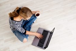 Frau mit Kaffee sitzt am Boden vor Laptop