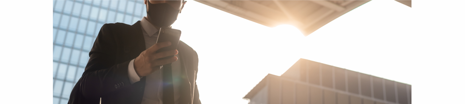 Businessman mit Maske vor Hochhäusern und Sonne Jobsuche im Sommer 2021